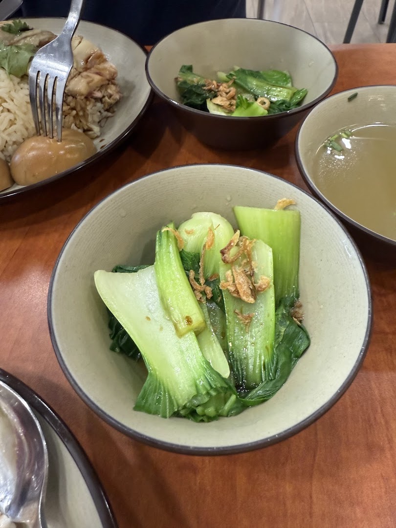 A delicious spread of Hainanese chicken rice, braised eggs, and fresh greens on a wooden table.