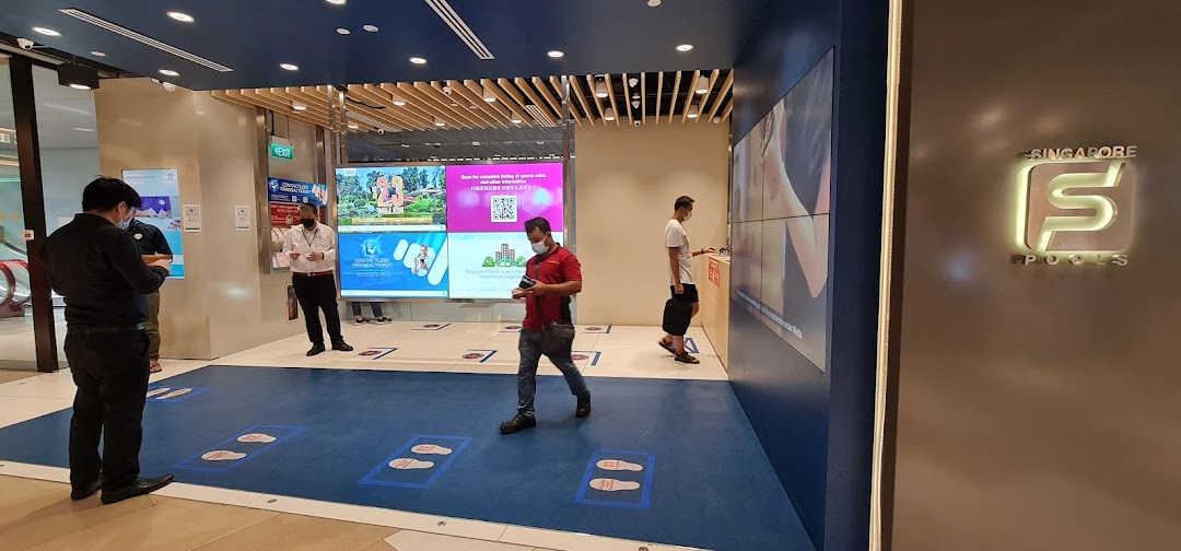 The entrance of Singapore Pools Funan Branch with customers, staff, and digital information displays.
