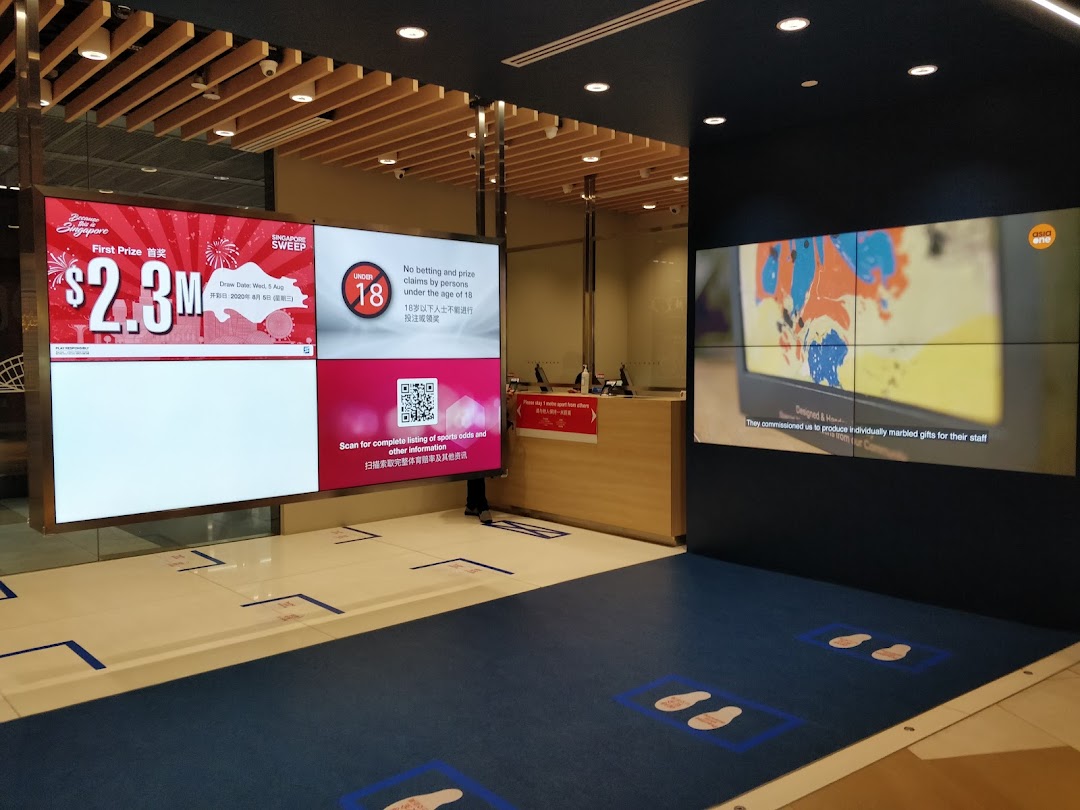 Interior view of Singapore Pools Funan Branch with large digital displays showing promotions and information.