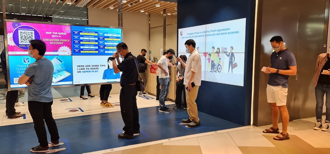 Customers queue at Singapore Pools Funan, viewing digital displays with information and safer play tips.