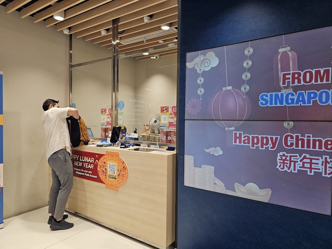 A customer at the counter of Singapore Pools Funan Branch with a festive digital display.
