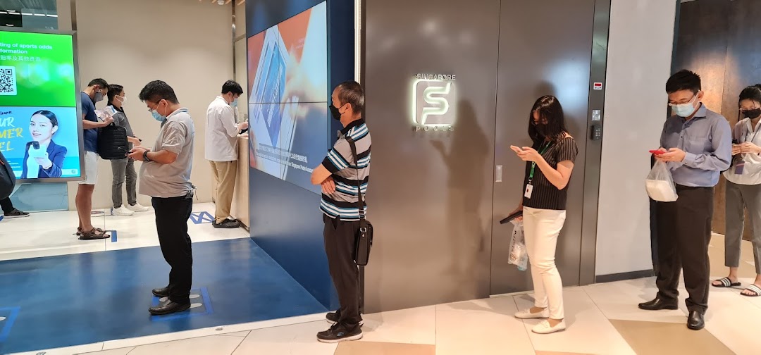 Customers queue patiently at the Singapore Pools Funan Branch, engaging with digital screens.