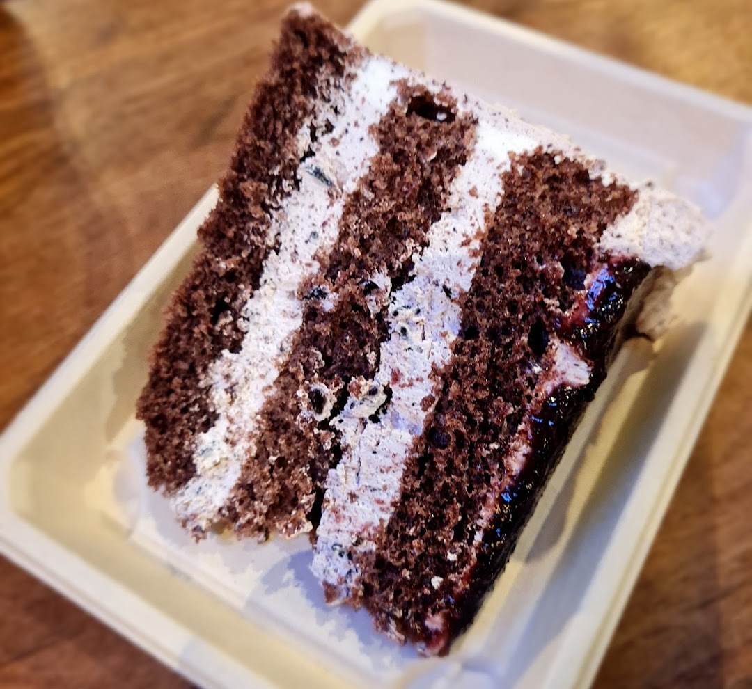 A close-up of a decadent chocolate cake slice with multiple cream layers and a fruit filling.