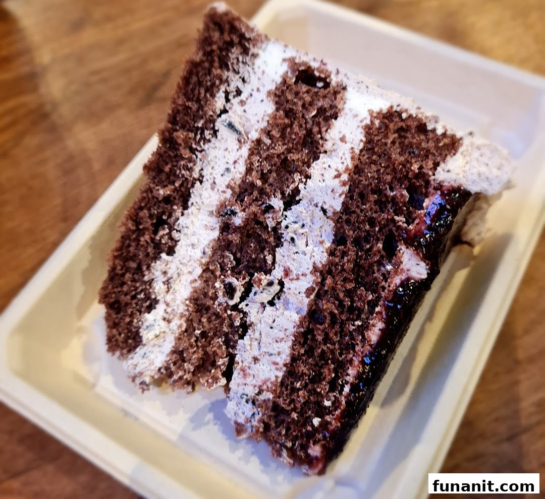 A close-up of a decadent chocolate cake slice with multiple cream layers and a fruit filling.