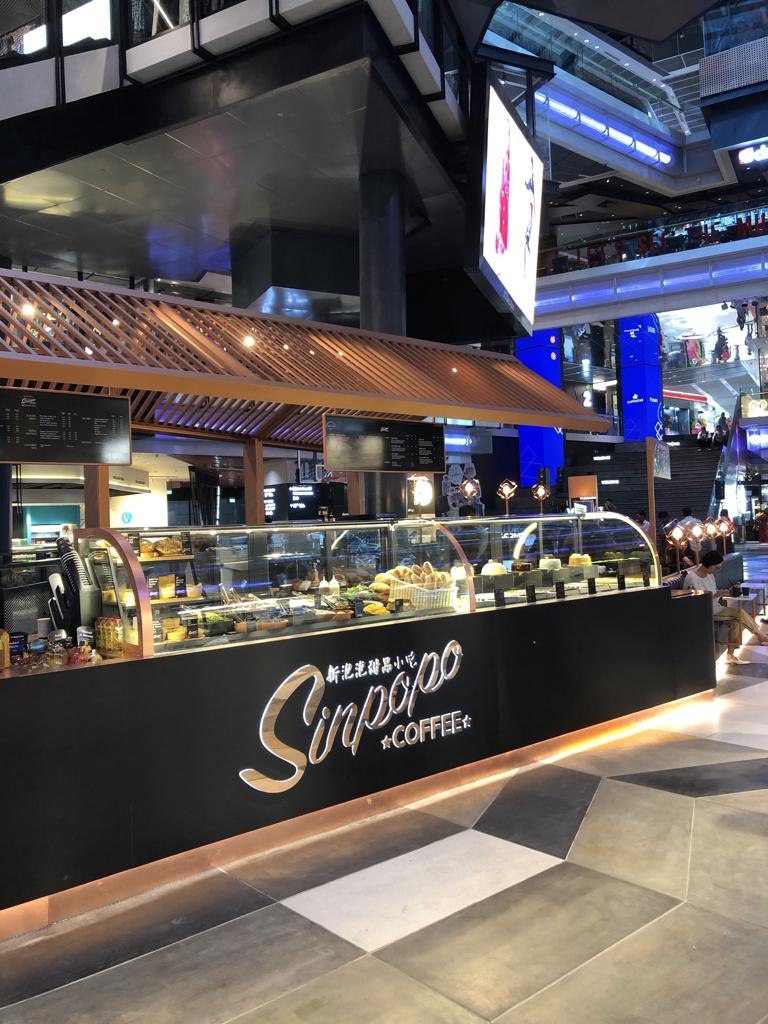 A modern Sinpopo Coffee counter with a display of pastries and cakes in a mall setting.