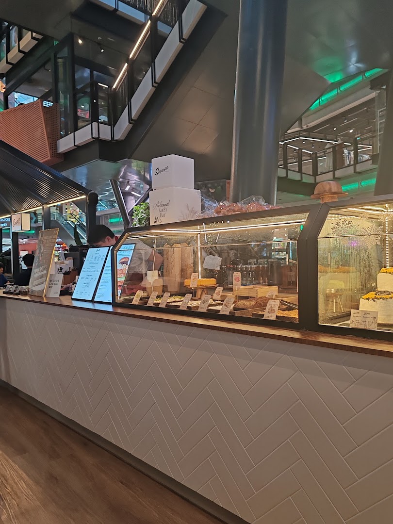 A view of Sinpopo Coffee's counter displaying pastries, cakes, and menu boards in a modern mall setting.