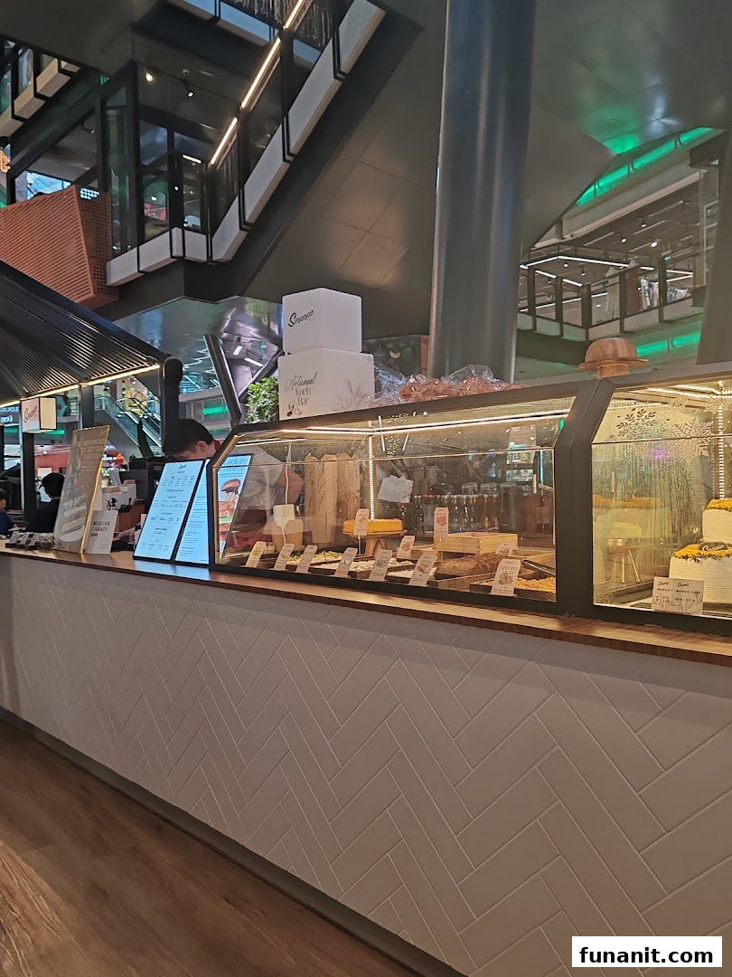 A view of Sinpopo Coffee's counter displaying pastries, cakes, and menu boards in a modern mall setting.