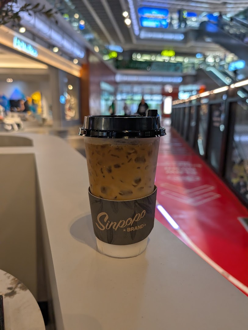 An iced coffee from Sinpopo Coffee with the mall interior and escalators in the background.