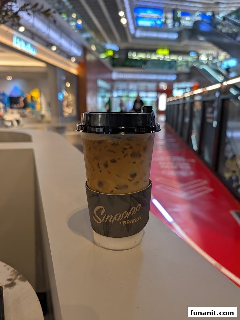 An iced coffee from Sinpopo Coffee with the mall interior and escalators in the background.
