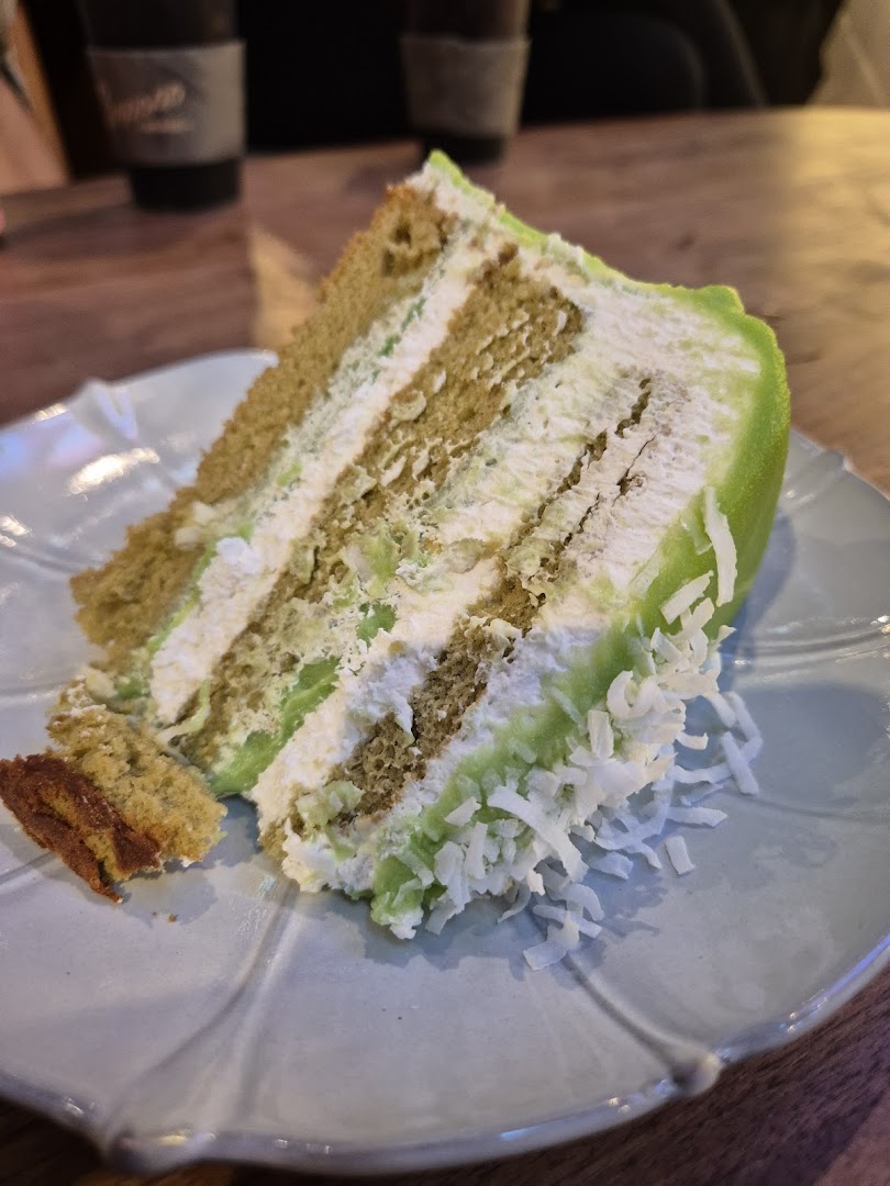 A vibrant slice of multi-layered cake with green frosting and coconut flakes on a light blue plate.