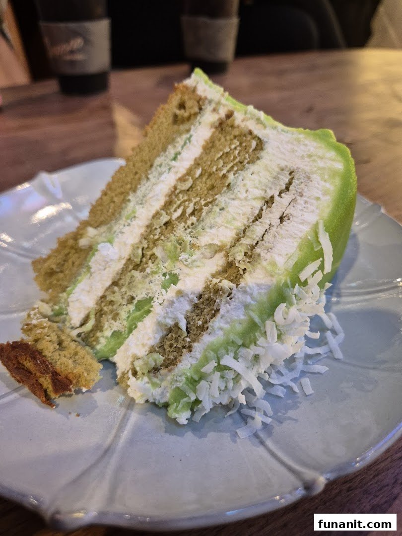 A vibrant slice of multi-layered cake with green frosting and coconut flakes on a light blue plate.