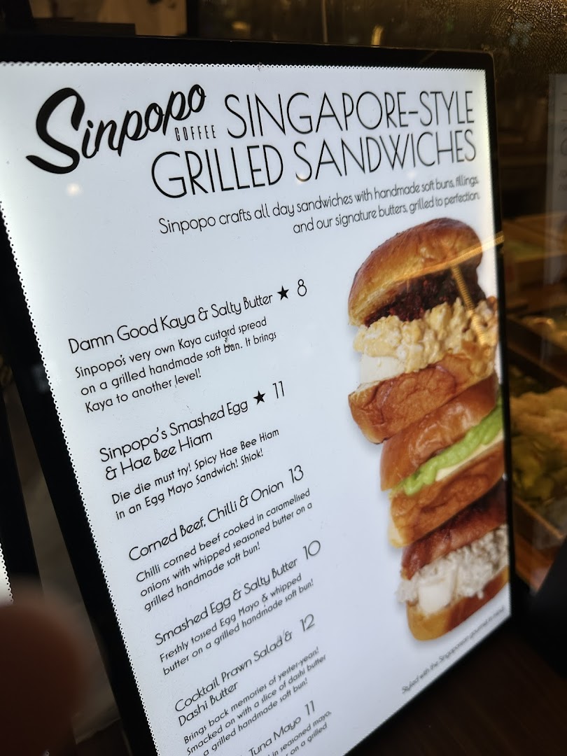 A brightly lit menu board displaying Sinpopo Coffee's Singapore-style grilled sandwiches.