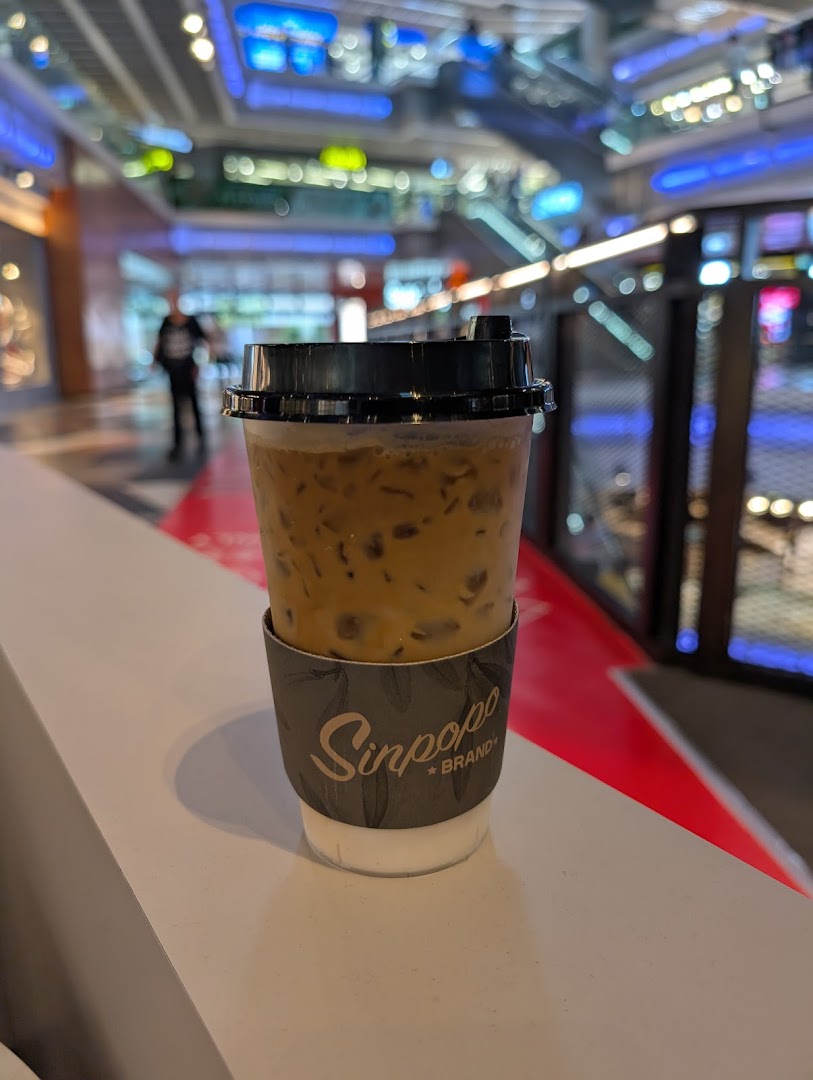An iced coffee from Sinpopo Coffee with its branded sleeve, set against a blurred mall background.