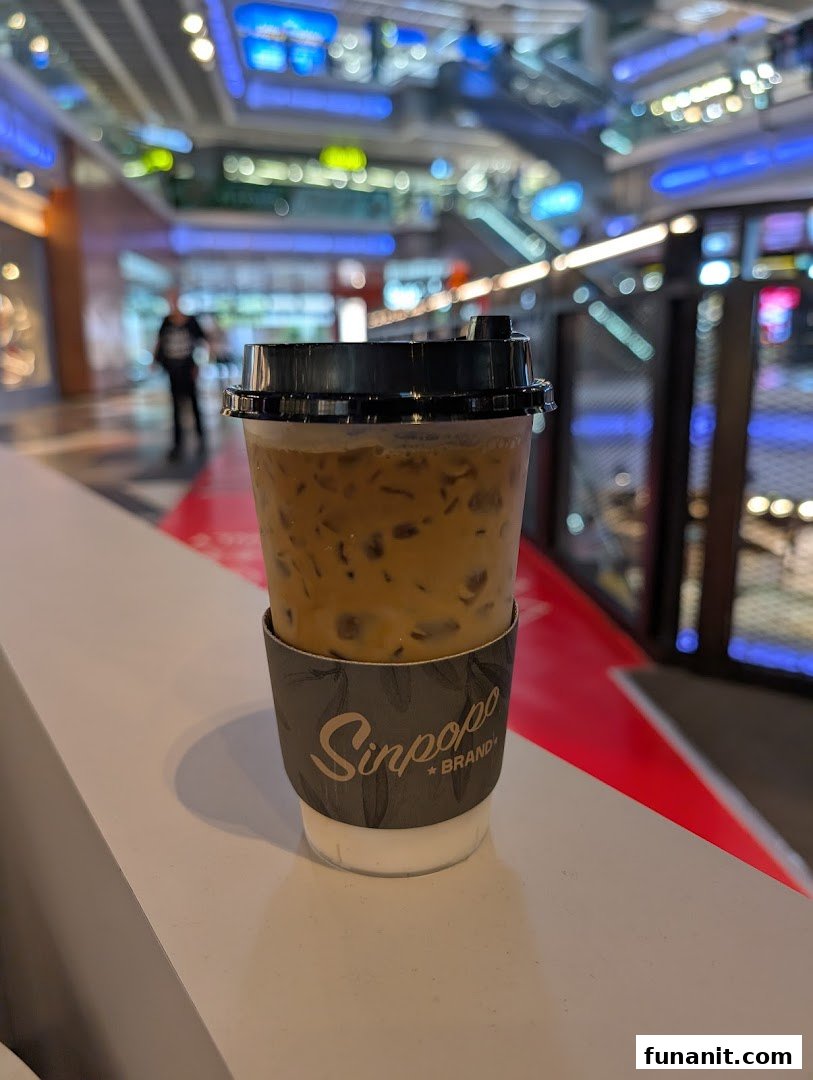 An iced coffee from Sinpopo Coffee with its branded sleeve, set against a blurred mall background.