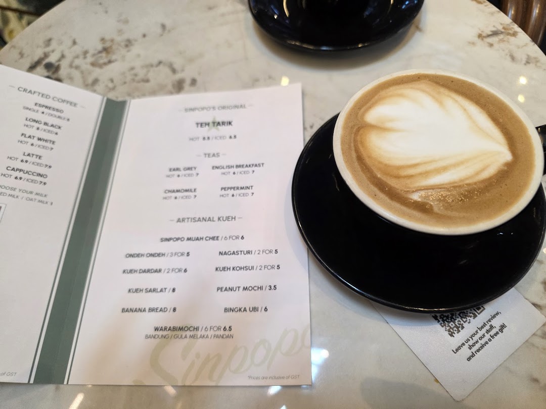 A menu displaying coffee, tea, and kueh options, with a latte art coffee cup on a marble table.