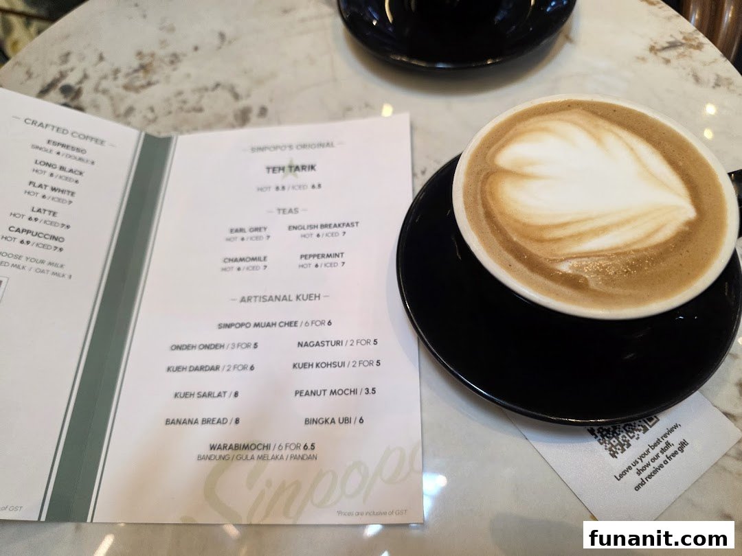 A menu displaying coffee, tea, and kueh options, with a latte art coffee cup on a marble table.