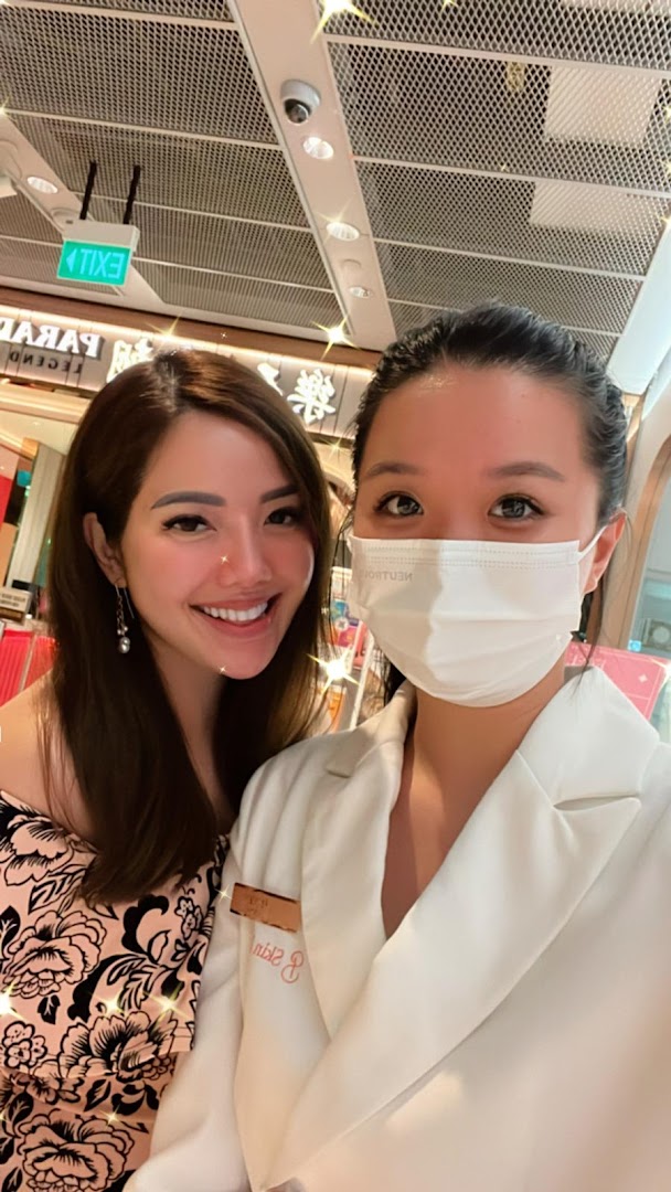 Two women, one smiling and one masked, posing inside the Skin Belief shop.