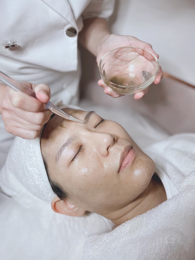 A person receiving a facial treatment with a mask being applied by a therapist.