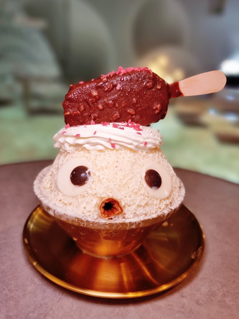 A cute character-themed shaved ice dessert topped with whipped cream, sprinkles, and a chocolate ice cream bar.