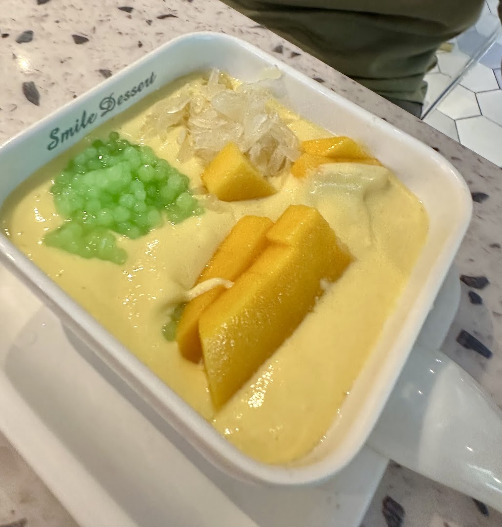 A vibrant mango dessert with green tapioca pearls and pomelo in a white bowl from Smile Dessert.