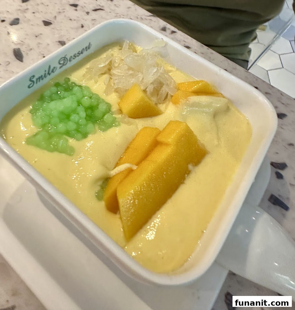 A vibrant mango dessert with green tapioca pearls and pomelo in a white bowl from Smile Dessert.