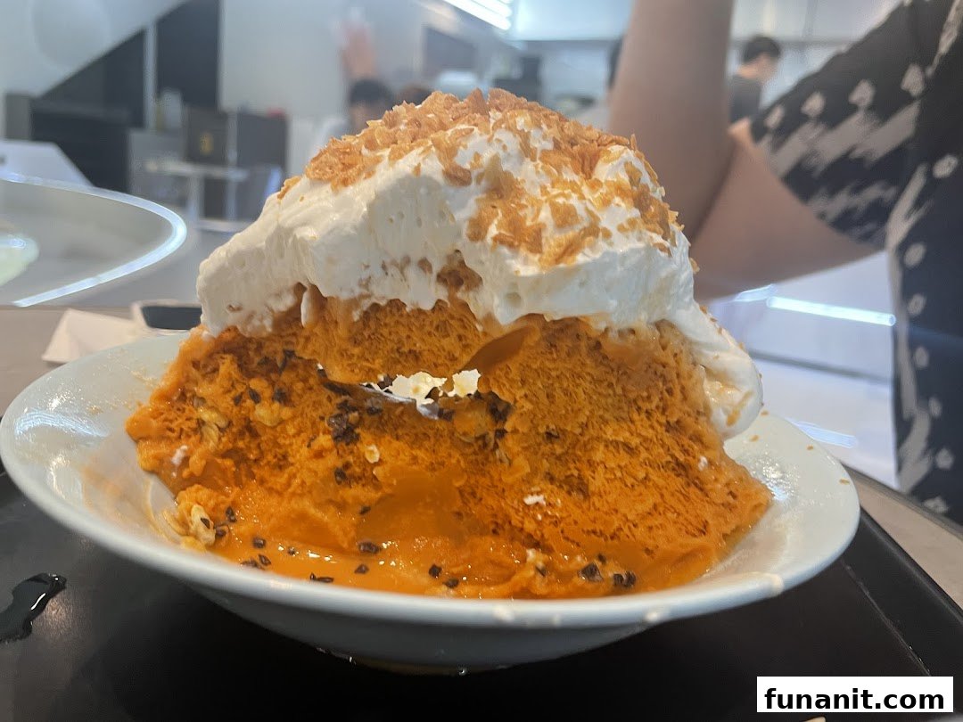 A large, vibrant orange shaved ice dessert topped with whipped cream and crunchy flakes.