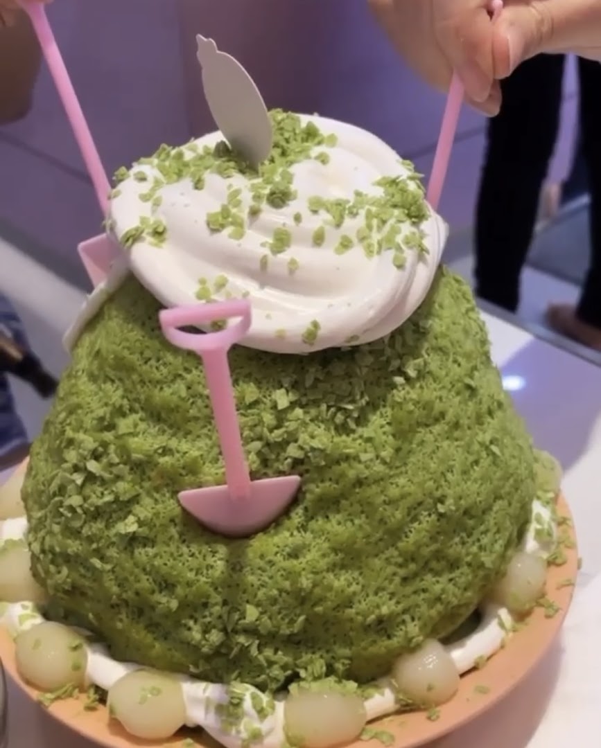 A large matcha-flavored shaved ice dessert topped with whipped cream and green sprinkles, served with small mochi.