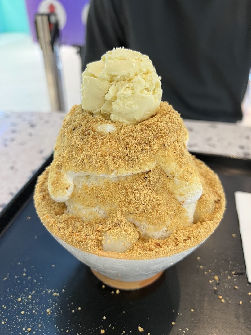 A large bowl of shaved ice dessert topped with ice cream, peanut powder, and mochi.
