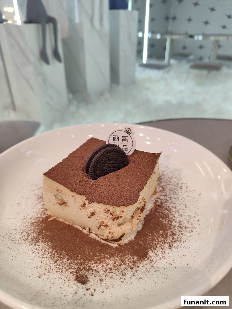 Decadent tiramisu-style dessert with cocoa and an Oreo on a white plate.