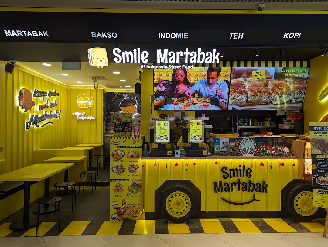 Vibrant yellow Smile Martabak shop front featuring a counter, seating, and screens showcasing Indonesian street food.