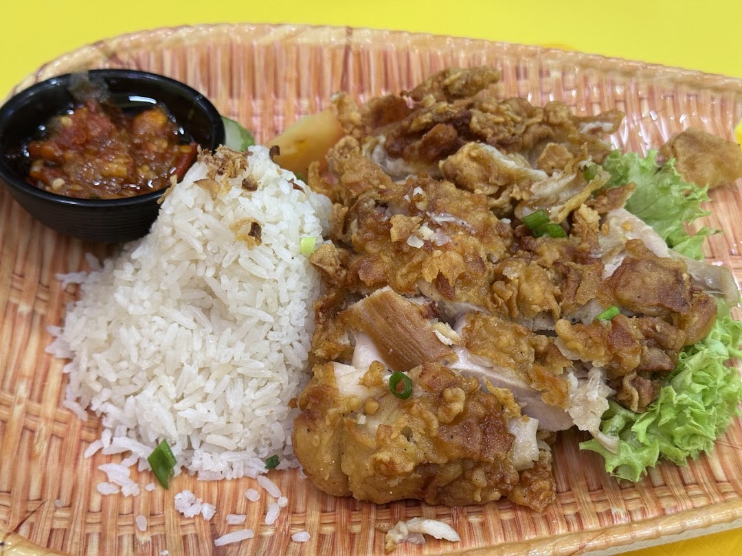 A close-up of crispy fried chicken with fragrant rice, fresh lettuce, and a side of spicy chili.