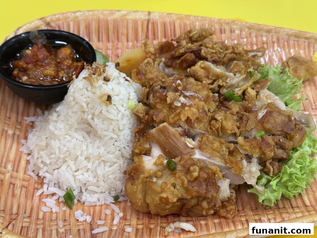 A close-up of crispy fried chicken with fragrant rice, fresh lettuce, and a side of spicy chili.