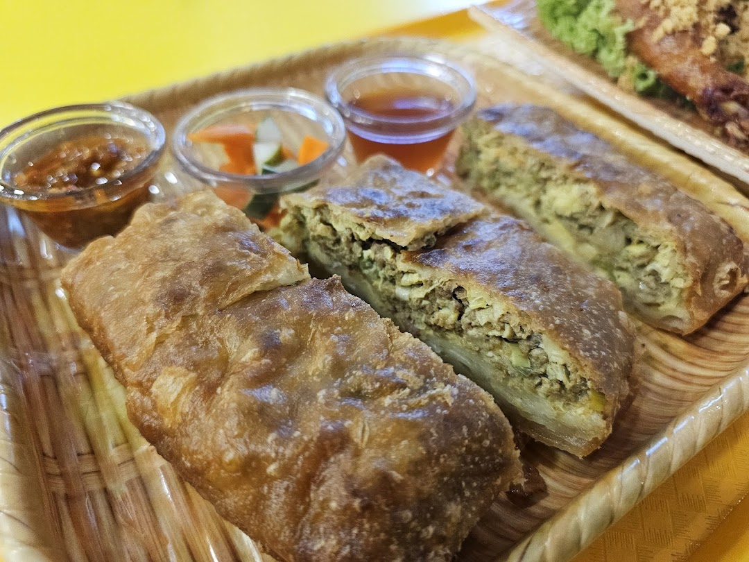Close-up of savory martabak slices served with chili sauce and pickled vegetables on a tray.