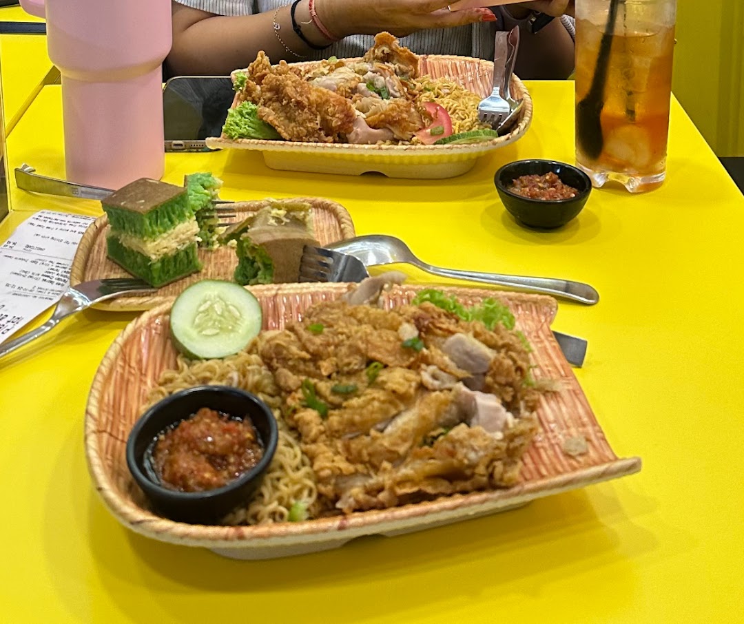 Two plates of crispy fried chicken noodles and a sweet martabak dessert served on a vibrant yellow table.