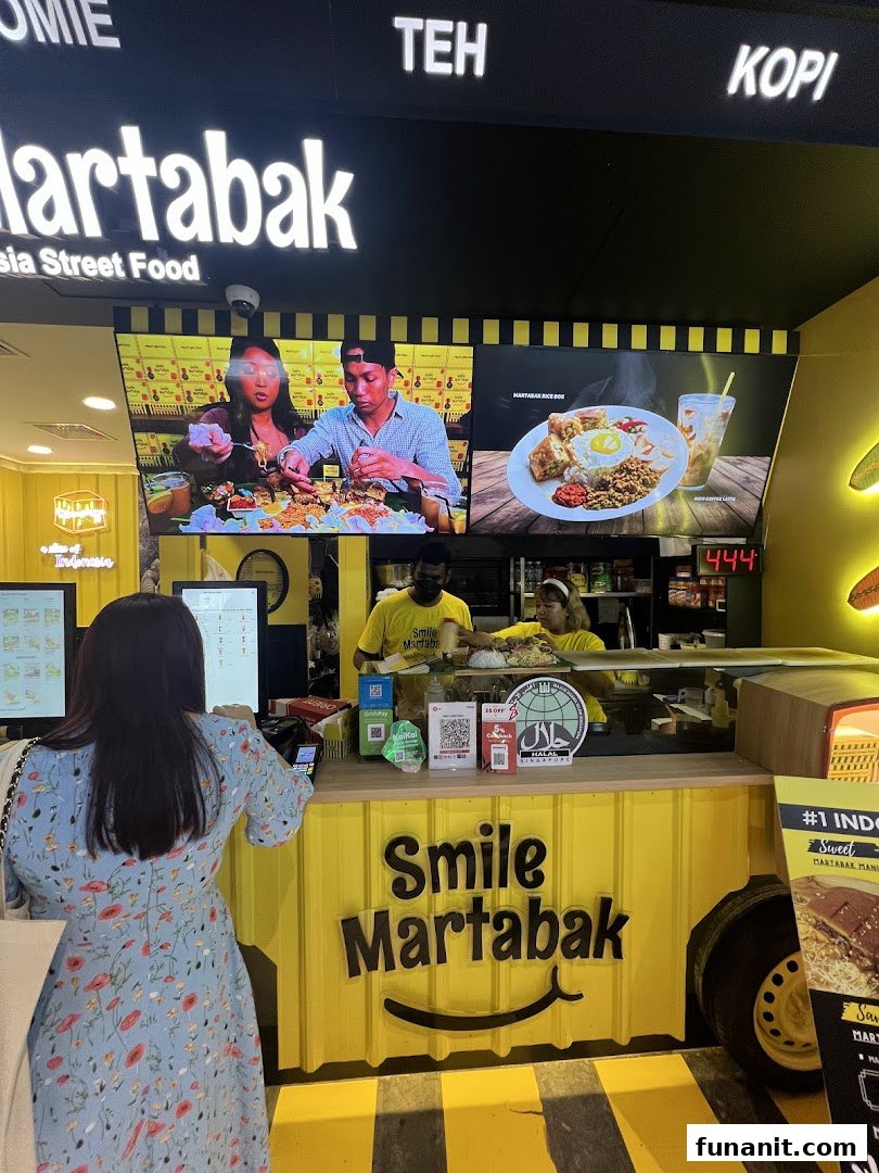 A customer orders at the vibrant yellow counter of Smile Martabak, an Indonesian street food stall.