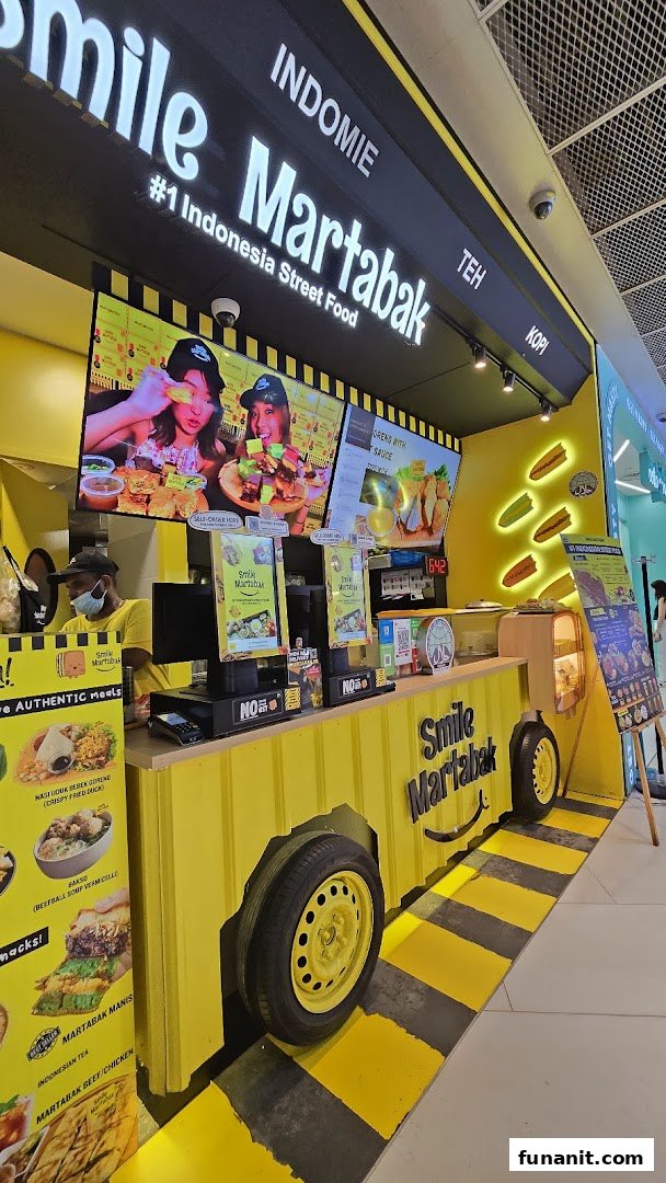 A vibrant yellow street food stall, Smile Martabak, featuring a truck-like design and digital menu displays.