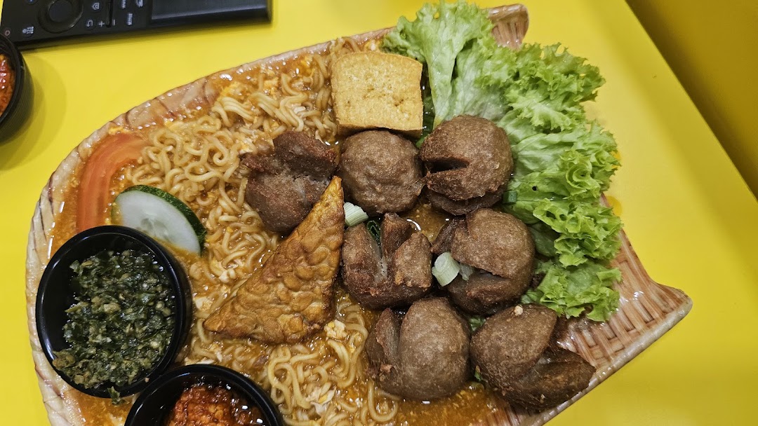 A close-up of a hearty meal featuring noodles, meatballs, tofu, tempeh, and fresh vegetables.
