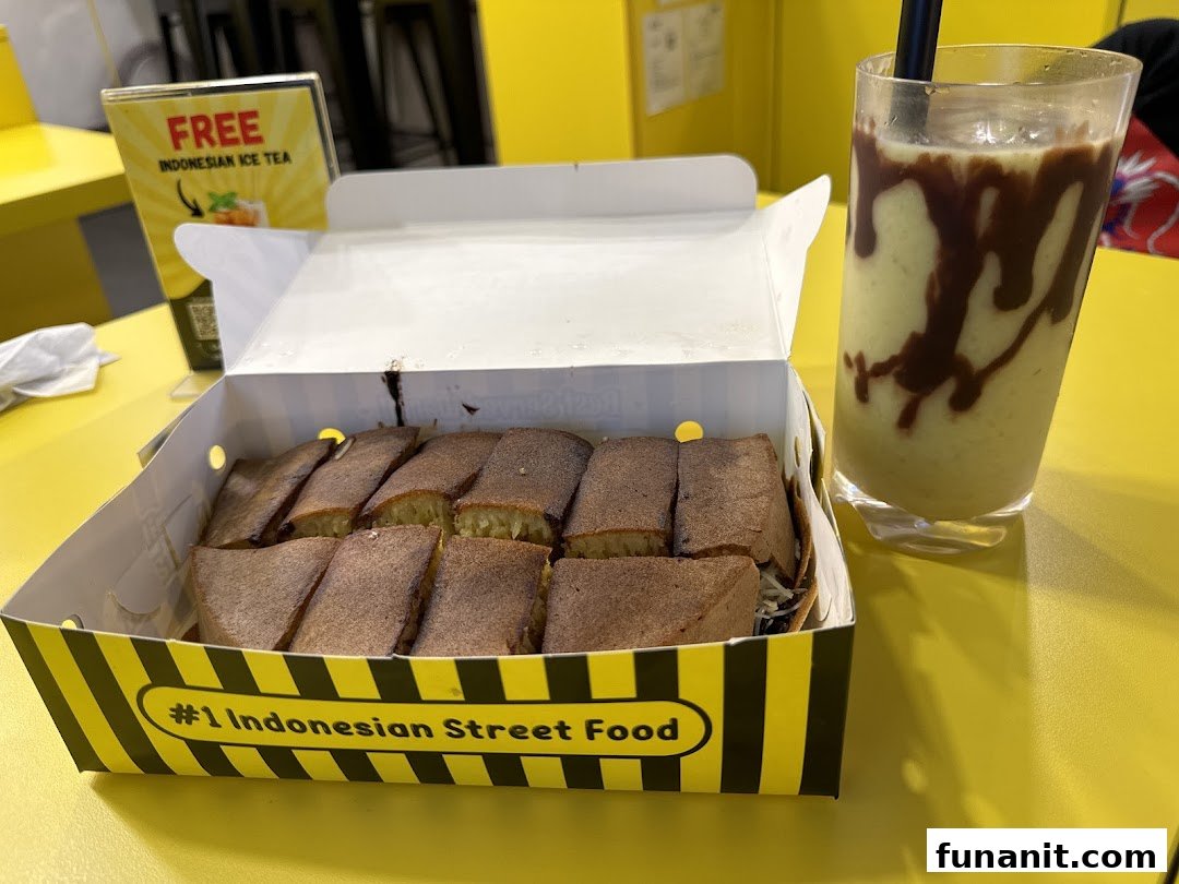 Delicious martabak slices in a box with a refreshing drink on a vibrant yellow table.