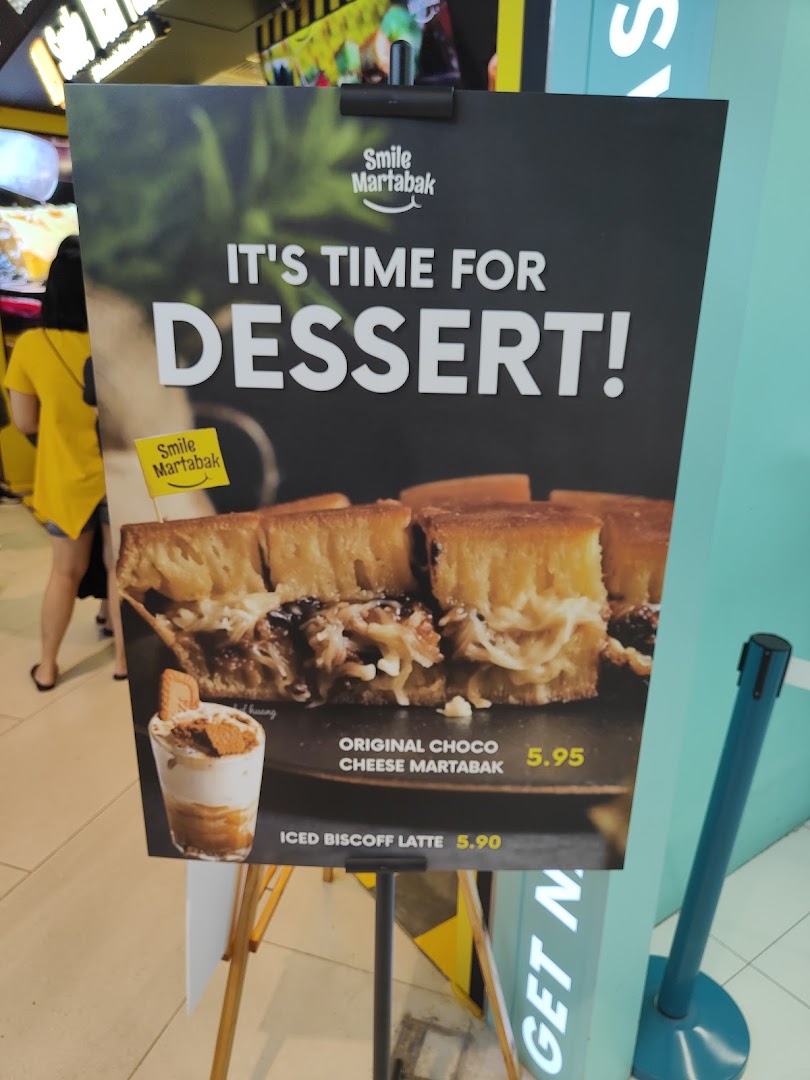 A promotional standee for Smile Martabak showcasing their Original Choco Cheese Martabak and Iced Biscoff Latte.