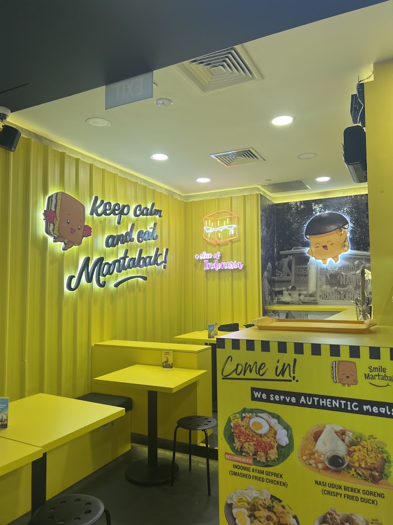 A vibrant interior shot of Smile Martabak, showcasing its yellow decor and a display board with authentic Indonesian meal options.