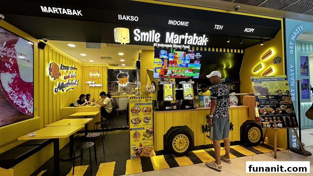 A vibrant yellow storefront of Smile Martabak, an Indonesian street food shop, with customers inside and a menu board outside.