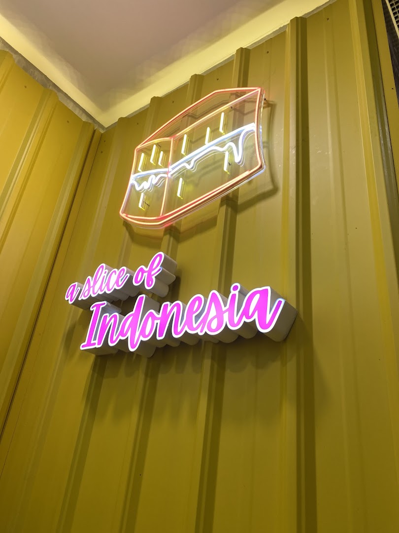 A neon sign depicting a martabak slice and text 'a slice of Indonesia' on a yellow corrugated wall.