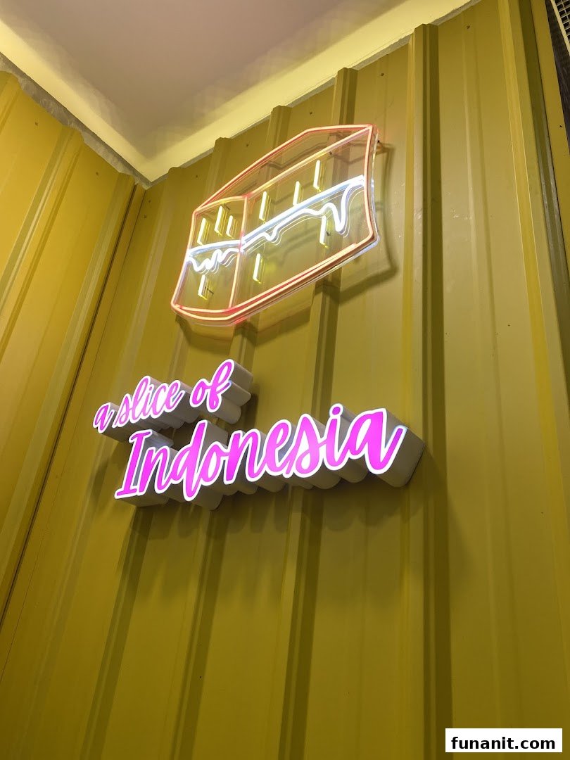 A neon sign depicting a martabak slice and text 'a slice of Indonesia' on a yellow corrugated wall.