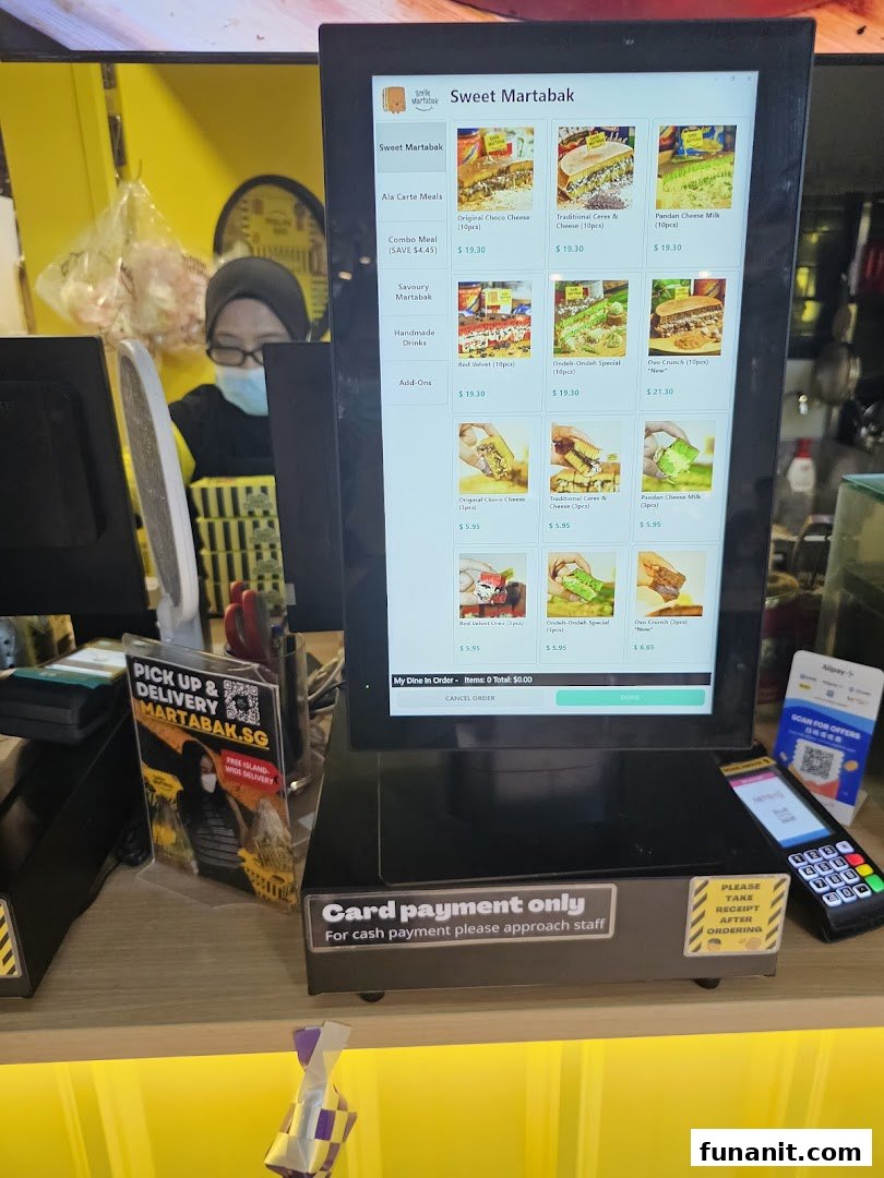 A digital menu display at a counter, showing various martabak options and prices, with a staff member in the background.
