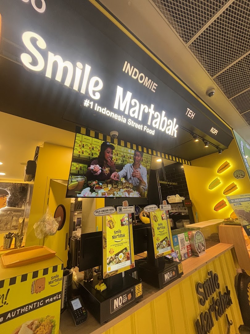Vibrant yellow and black shop front of Smile Martabak, featuring a large screen and self-order kiosks.