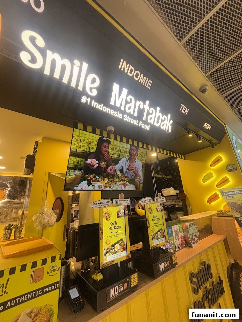 Vibrant yellow and black shop front of Smile Martabak, featuring a large screen and self-order kiosks.