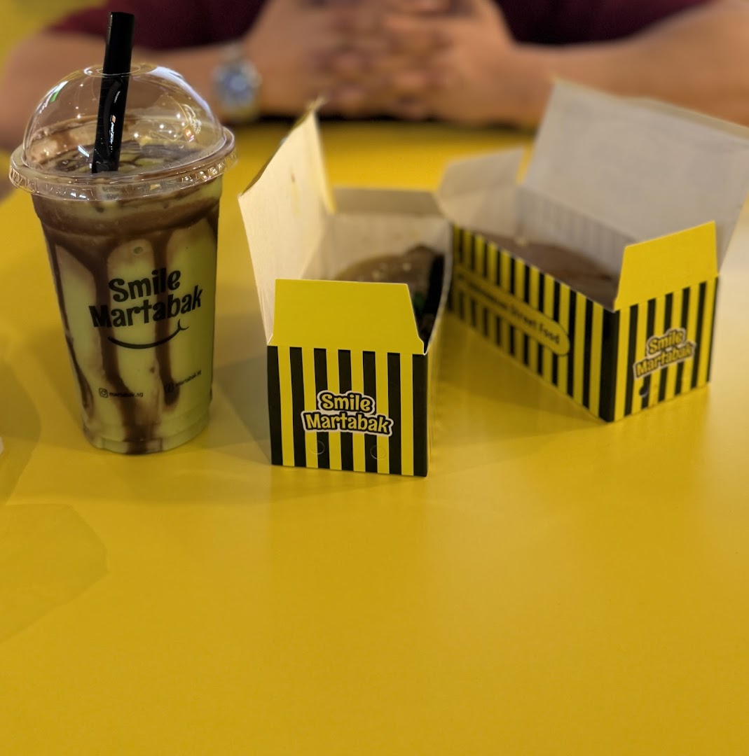 A refreshing drink and two boxes of martabak from Smile Martabak on a yellow table.
