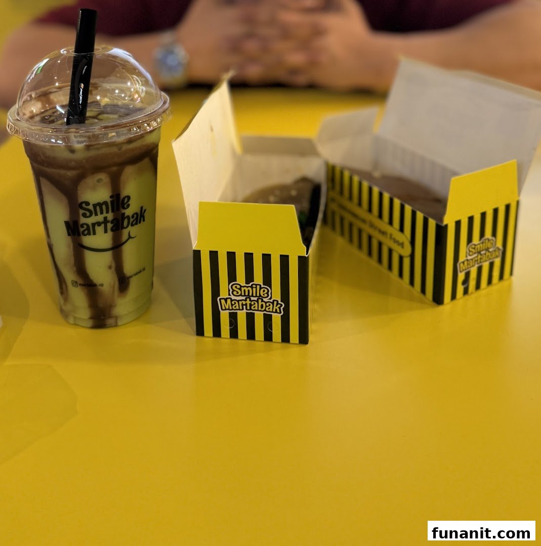 A refreshing drink and two boxes of martabak from Smile Martabak on a yellow table.