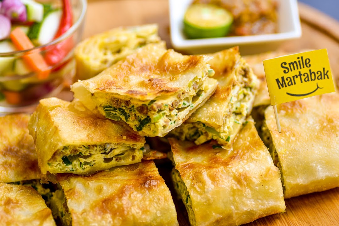 Deliciously golden martabak slices, served with a Smile Martabak flag and side condiments.