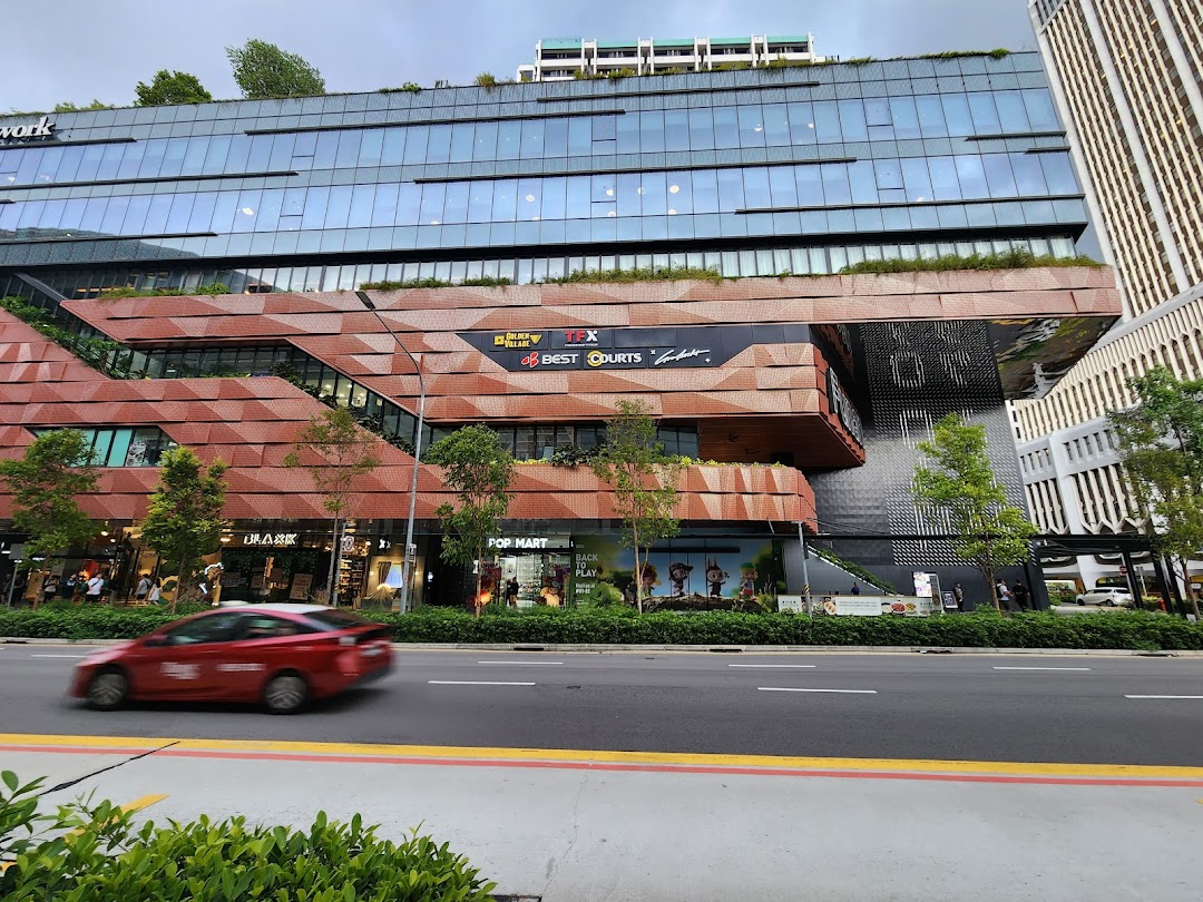A modern shopping complex exterior with multi-level retail spaces, a street, and a red car passing by.